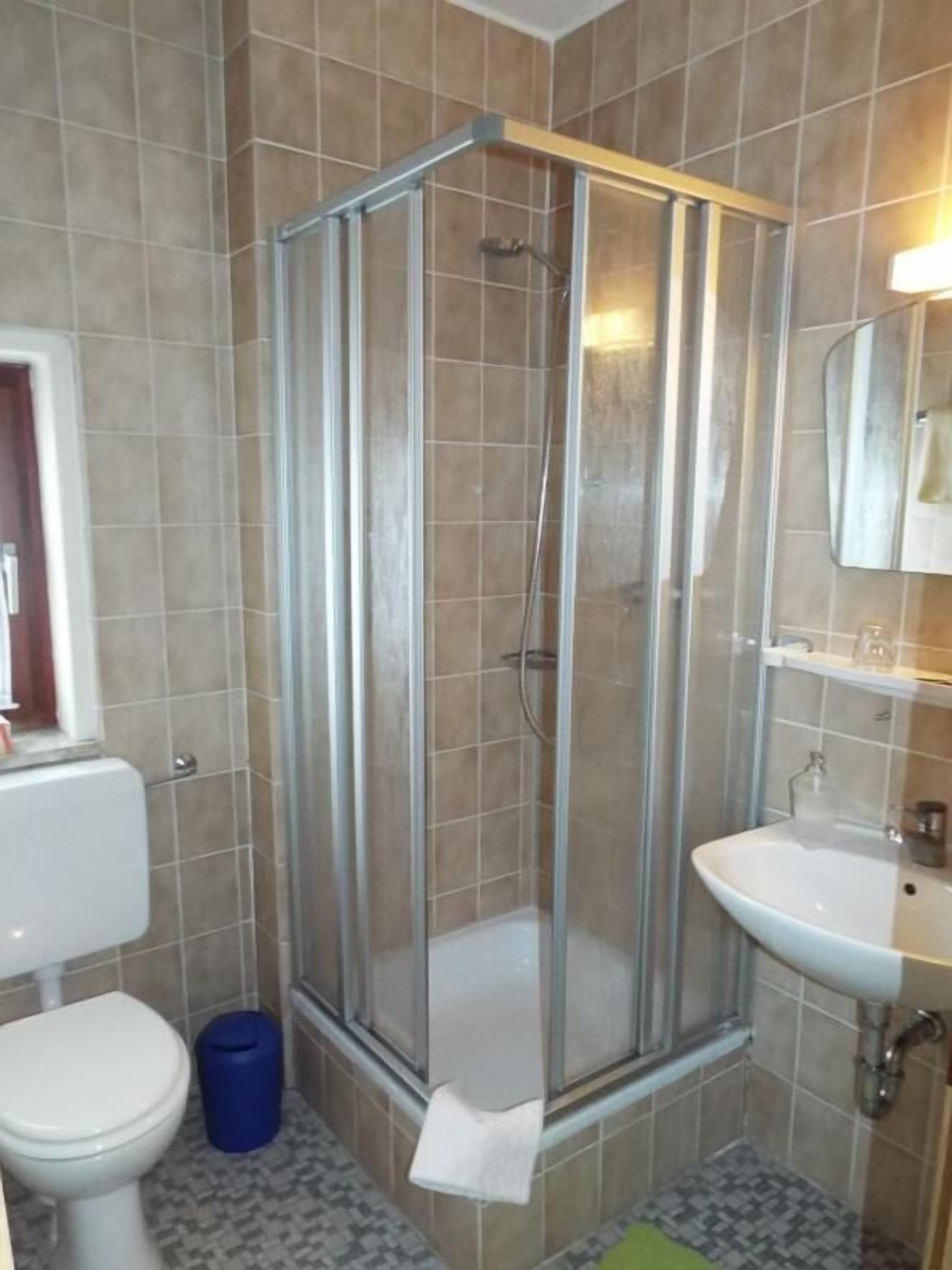 Un baño con ducha envuelta en vidrio, un lavamanos blanco y un inodoro.