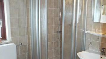 Un baño con ducha envuelta en vidrio, un lavamanos blanco y un inodoro.