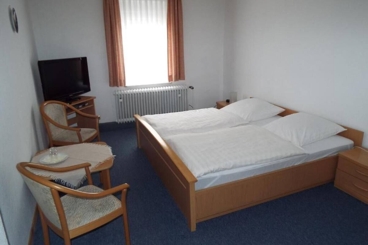 Una habitación de hotel con cama, televisión, una silla y una mesita.