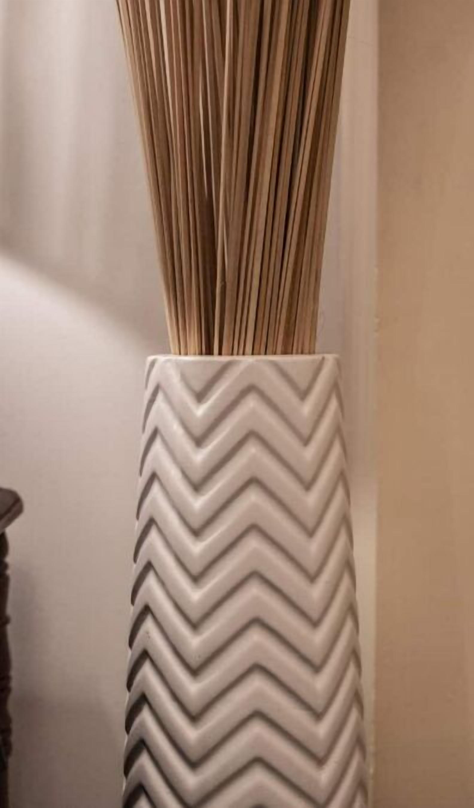 A white vase with a zigzag pattern containing a bunch of sticks.