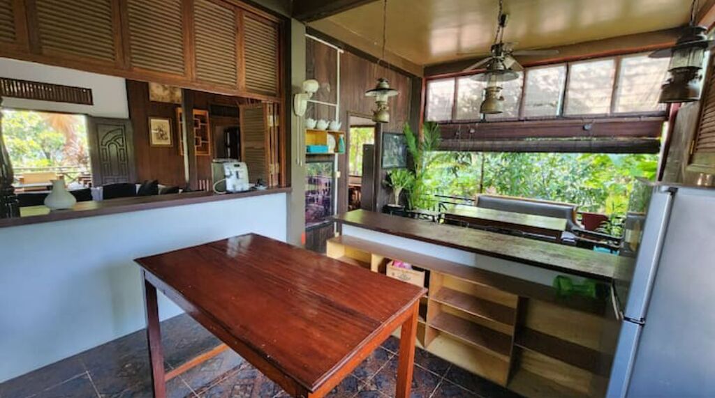A kitchen with a wooden table, a refrigerator, and a window with a view of greenery.