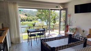 Habitación de hotel con balcón, una mesa de comedor con sillas, cama con cubrecama a cuadros y televisor montado en la pared.