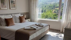 A bedroom with a large bed, a view of greenery outside, and a wooden floor. - Casa da Flor 3 (Amarante)