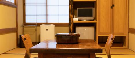 A traditional Japanese room with tatami mat flooring, a wooden table with a dark wooden bowl, and a television on a shelf.
