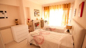 Quarto de hotel com duas camas, uma escrivaninha, uma cadeira, um penteado, um vaso com flores e um quadro na parede.