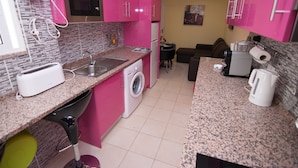 Uma cozinha compacta com armários rosa, micro-ondas, máquina de lavar e cafeteira.