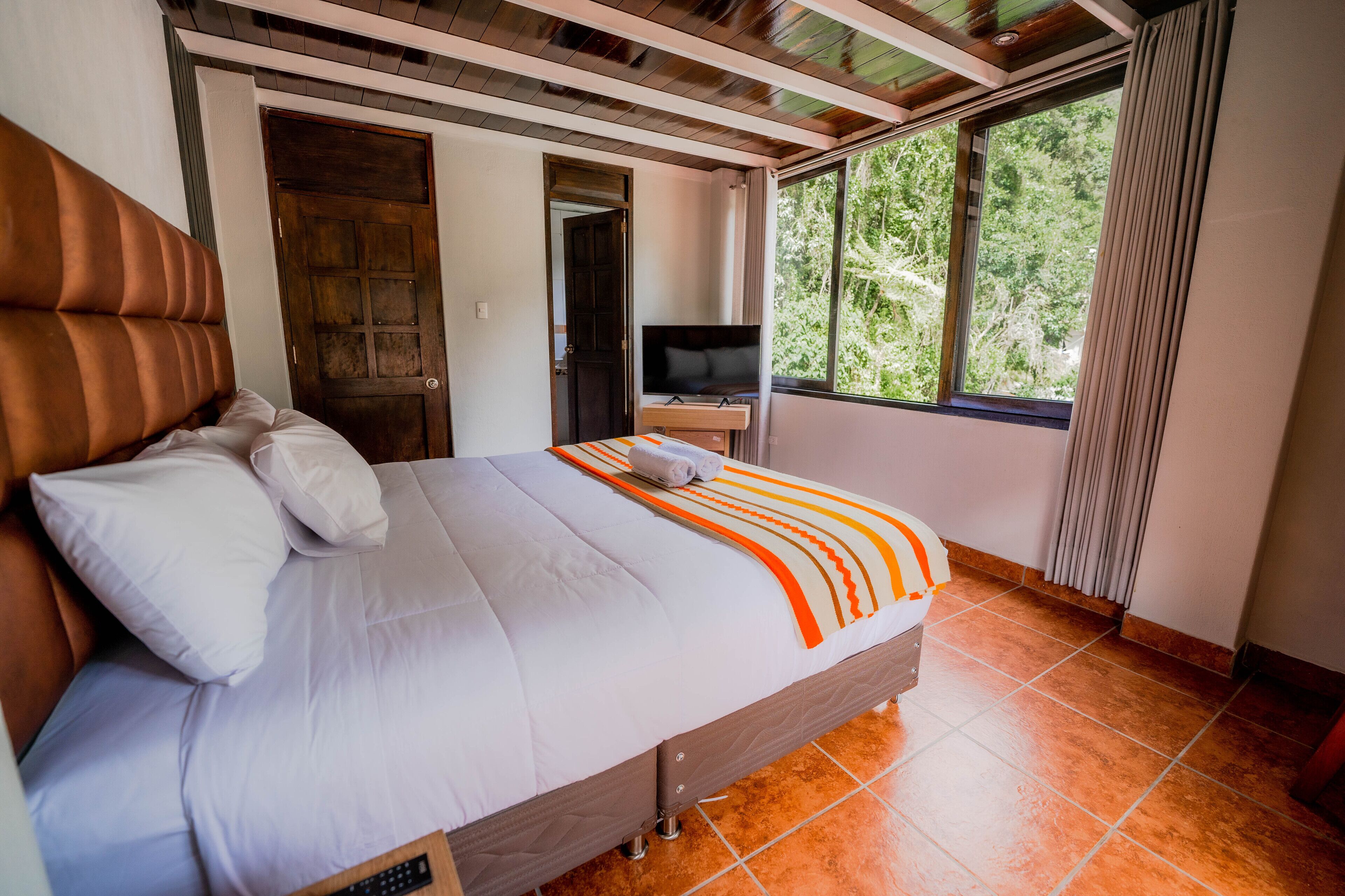 A bedroom with a large bed, a TV, and a window with a view of trees.