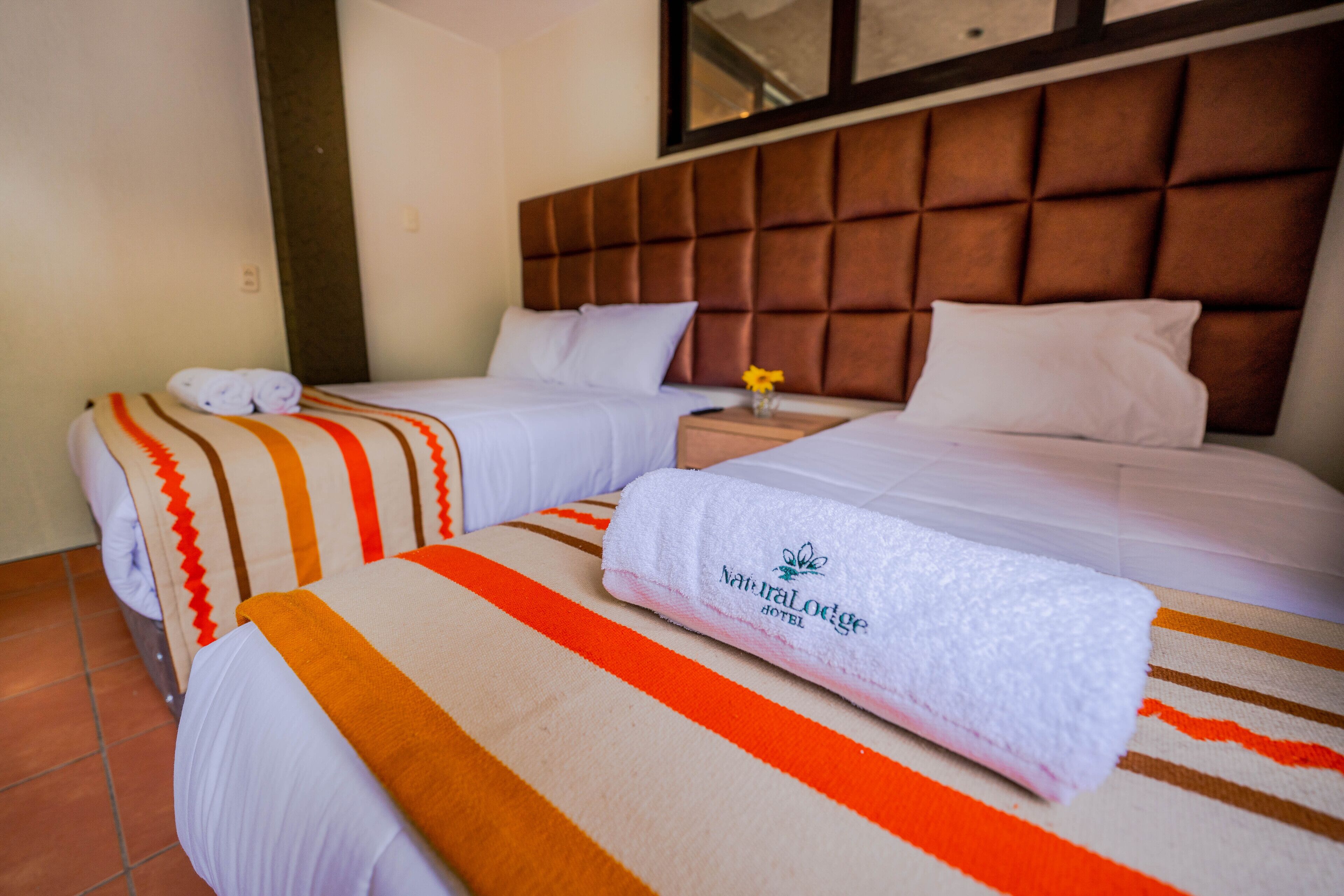 A hotel room with two beds, each with a striped bedspread and a rolled towel.