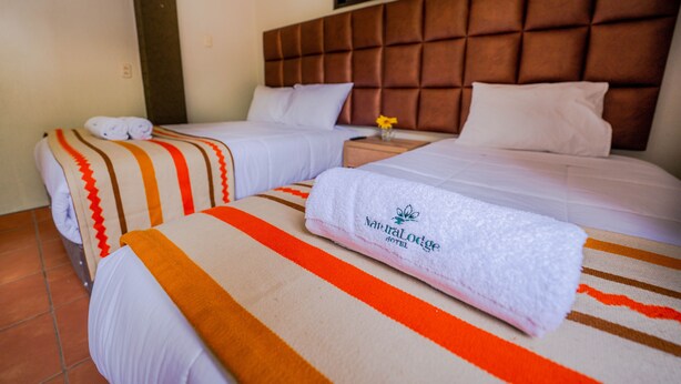 Habitación de hotel con dos camas, cada una con una colcha a rayas y una toalla enrollada.