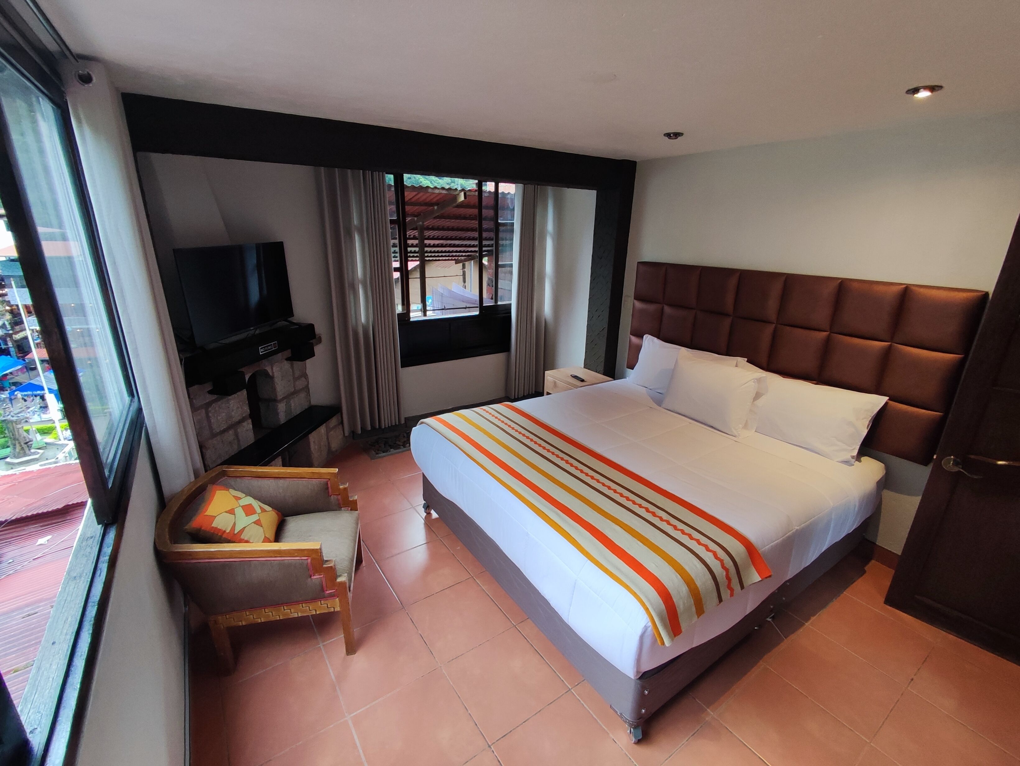 Habitación de hotel con una cama grande, televisión, un rincón de descanso y una ventana con cortinas.