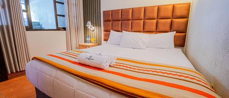 A hotel room with a large bed, a headboard, a nightstand, a lamp, and a window with curtains.