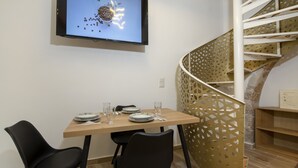 Un'area pranzo con un tavolo di legno apparecchiato per due persone, una TV fissata al muro e una scala a chiocciola con ringhiera in legno.