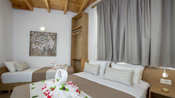 Una camera d'albergo con due letti, un soffitto in legno, un quadro appeso al muro e un'ampia finestra con tende.