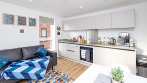 A modern kitchen with white cabinets, a built-in oven, and a microwave. There is a grey sofa with a blue and white patterned throw blanket.