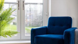 A blue armchair by a window with a view of a green landscape.