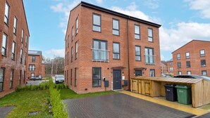 A multi-story brick building with a flat roof, a small garden area, and a wooden structure on the ground floor.