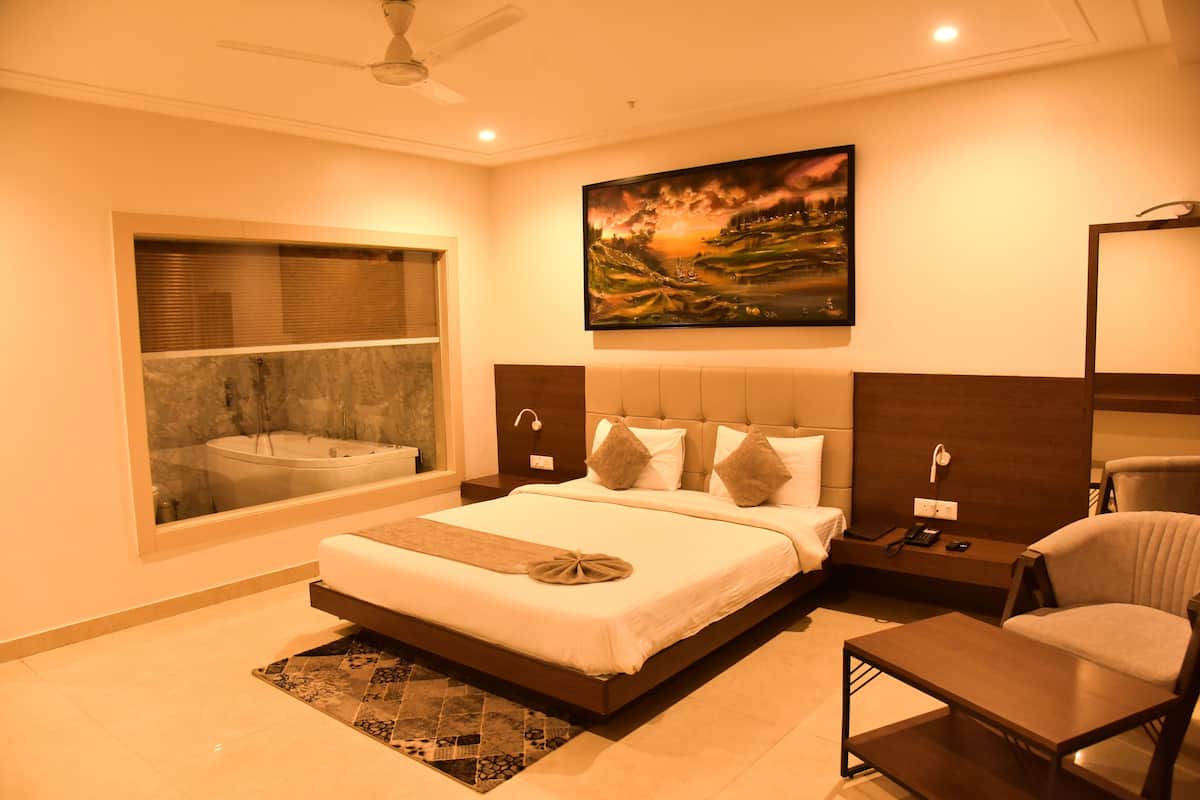 A hotel room with a large bed, a sitting area, a window with a view, a painting on the wall, and a ceiling fan.