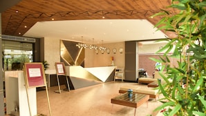 A modern hotel lobby with a reception desk, a seating area, and a decorative wall with clocks. - SWARNA HOTEL & RESORT (Kanthi)