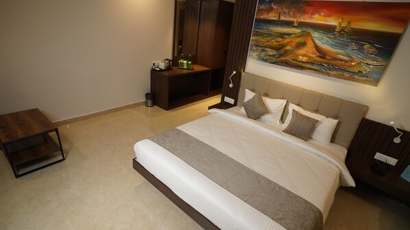 A neatly arranged hotel room with a large bed, a bedside table, a small side table, a wardrobe, and a painting of a coastal scene.