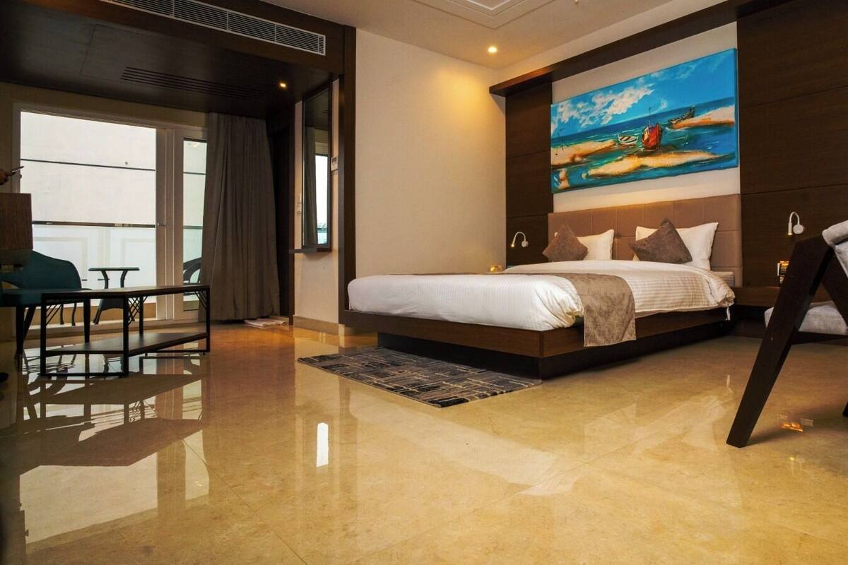 A hotel room with a bed, a desk, a chair, and a painting of a boat on a beach.