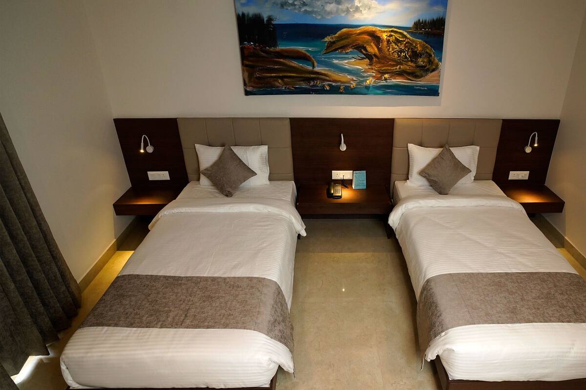A hotel room with two beds, a painting above, and a nightstand with a phone and a sign.