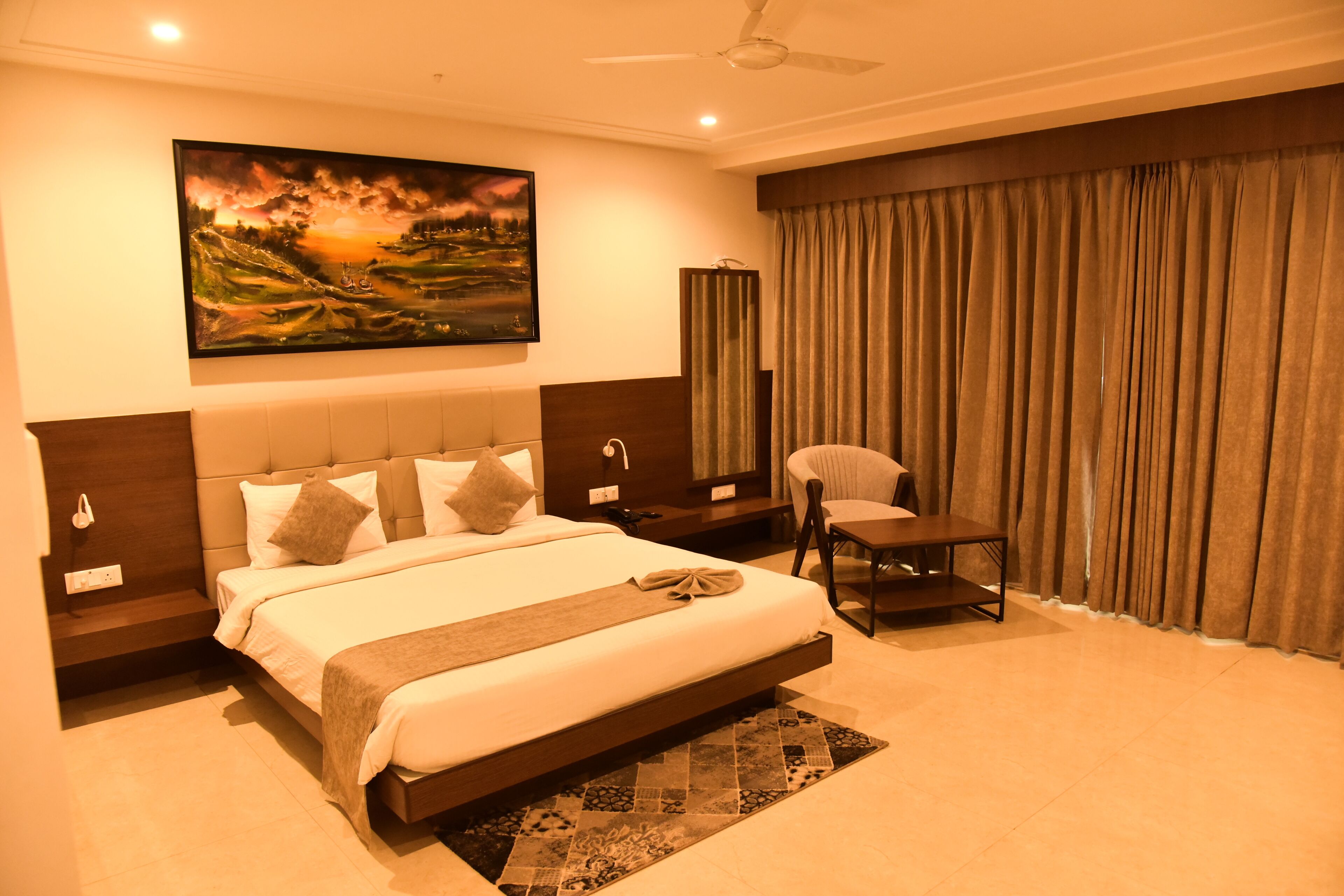 A hotel room with a large bed, a chair, a painting on the wall, and a curtain.