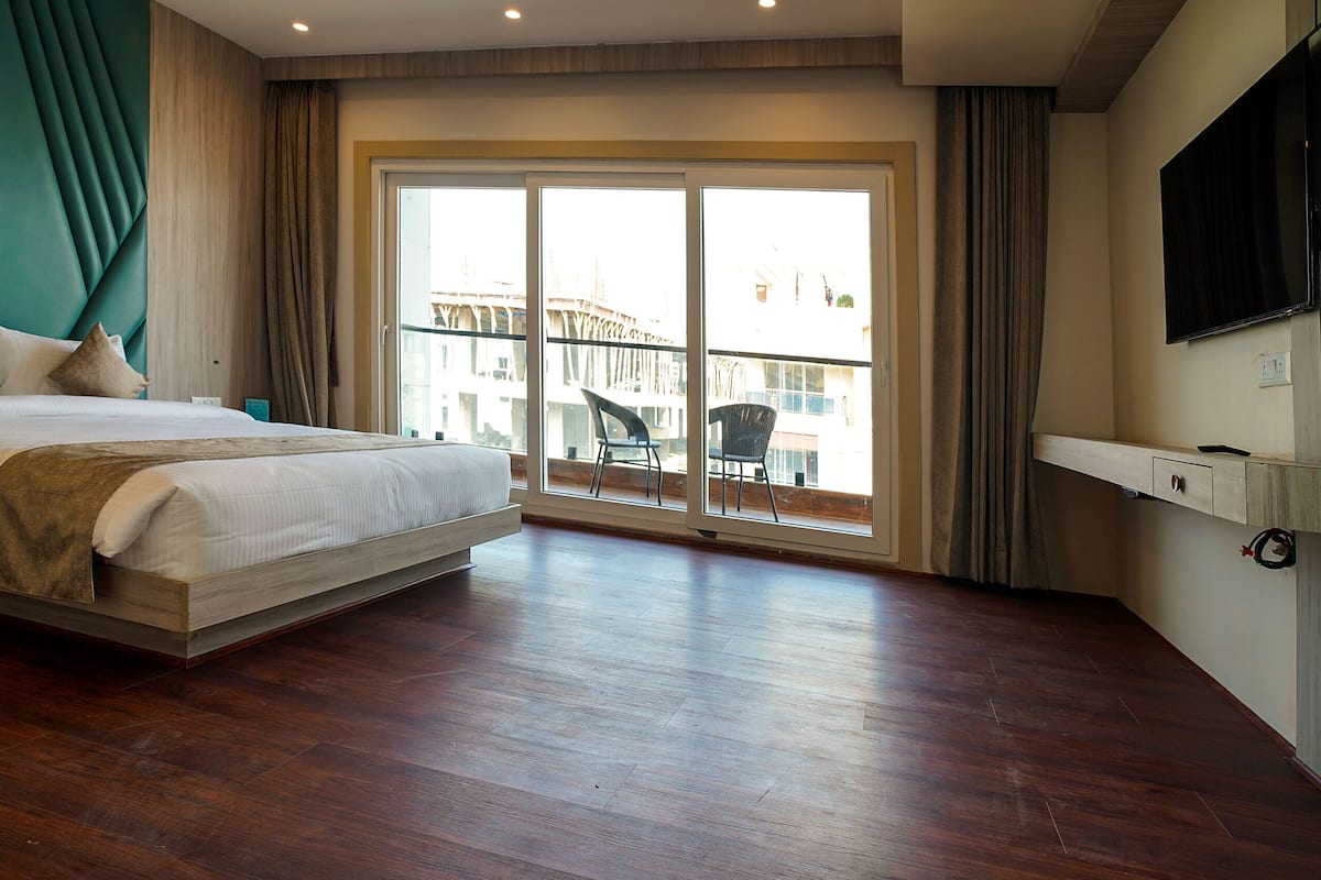 A modern hotel room with a large bed, a balcony with a chair, and a TV mounted on the wall.