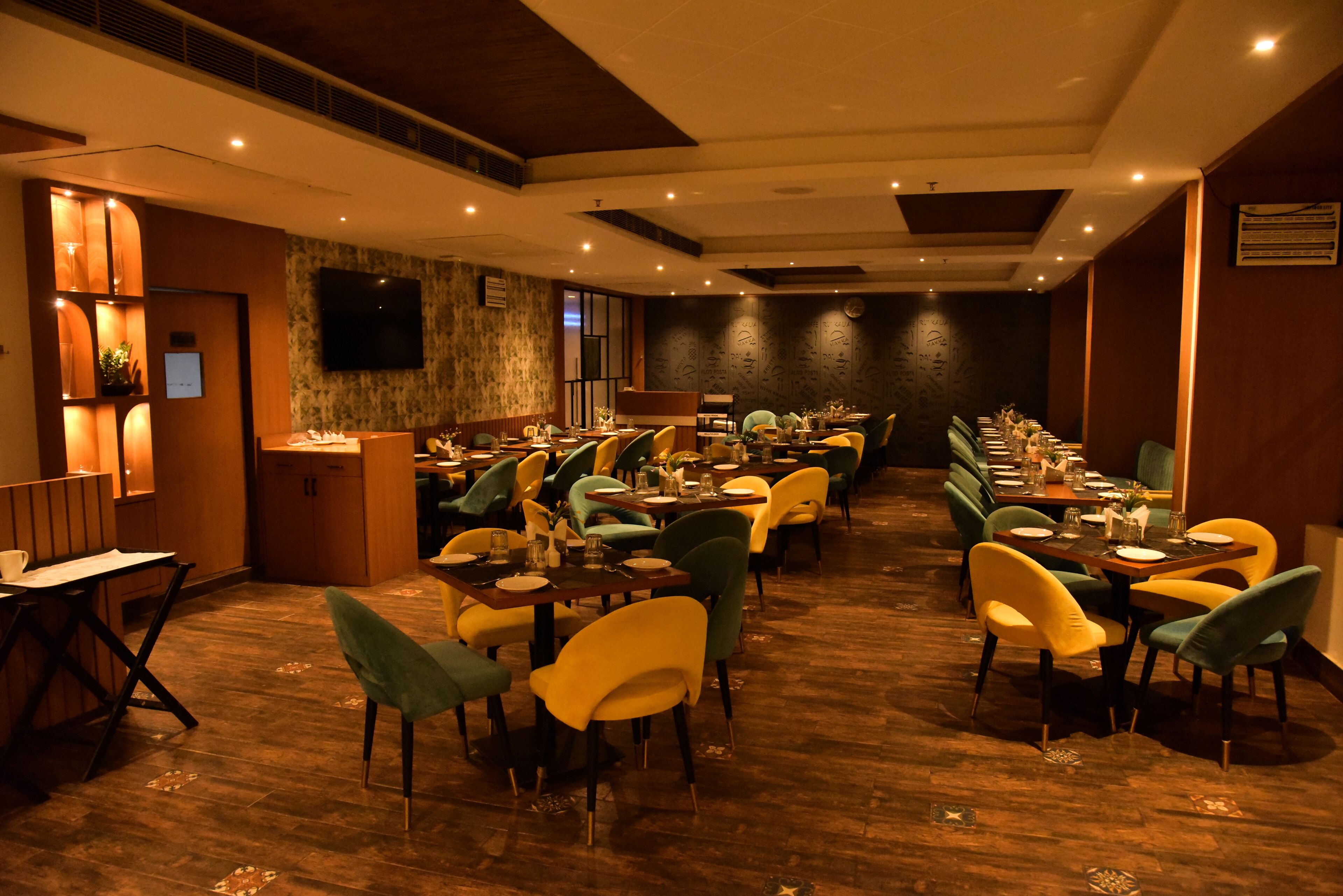 A restaurant with multiple tables and chairs, a television mounted on the wall, and a wooden floor.