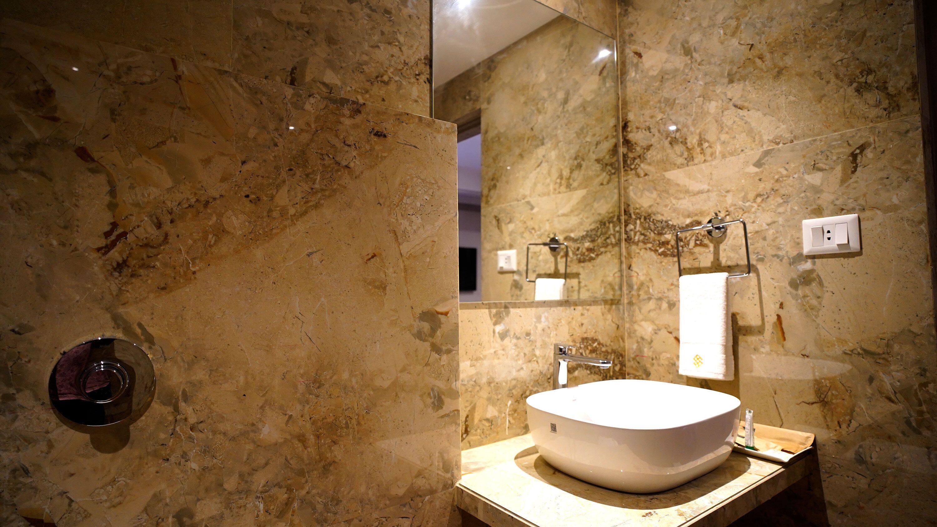 A bathroom with a marble wall, a sink, and a mirror.