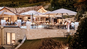 Un espacio de comedor al aire libre con paredes de ladrillo, varias mesas y sillas, y sombrillas que ofrecen sombra.