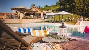 Zona de piscina con sillones reclinables, sombrillas y un bar junto a la piscina.