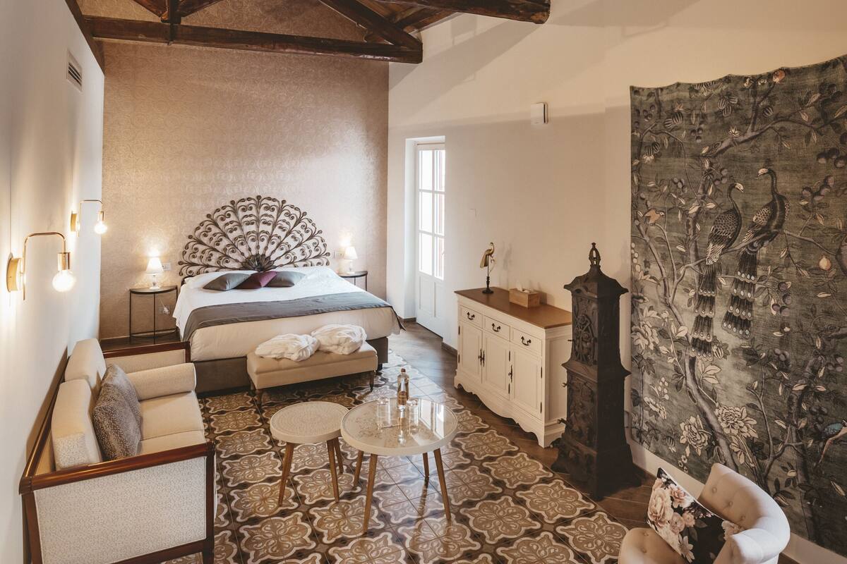 A bedroom with a wooden ceiling, a bed with a decorative headboard, a nightstand, a dresser, a tapestry, and a patterned rug.
