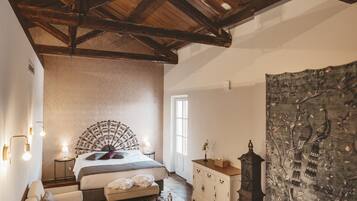 Un dormitorio con techo de madera, una cama con cabecera decorativa, una mesita de noche, un aparador, un tapiz y una alfombra estampada.