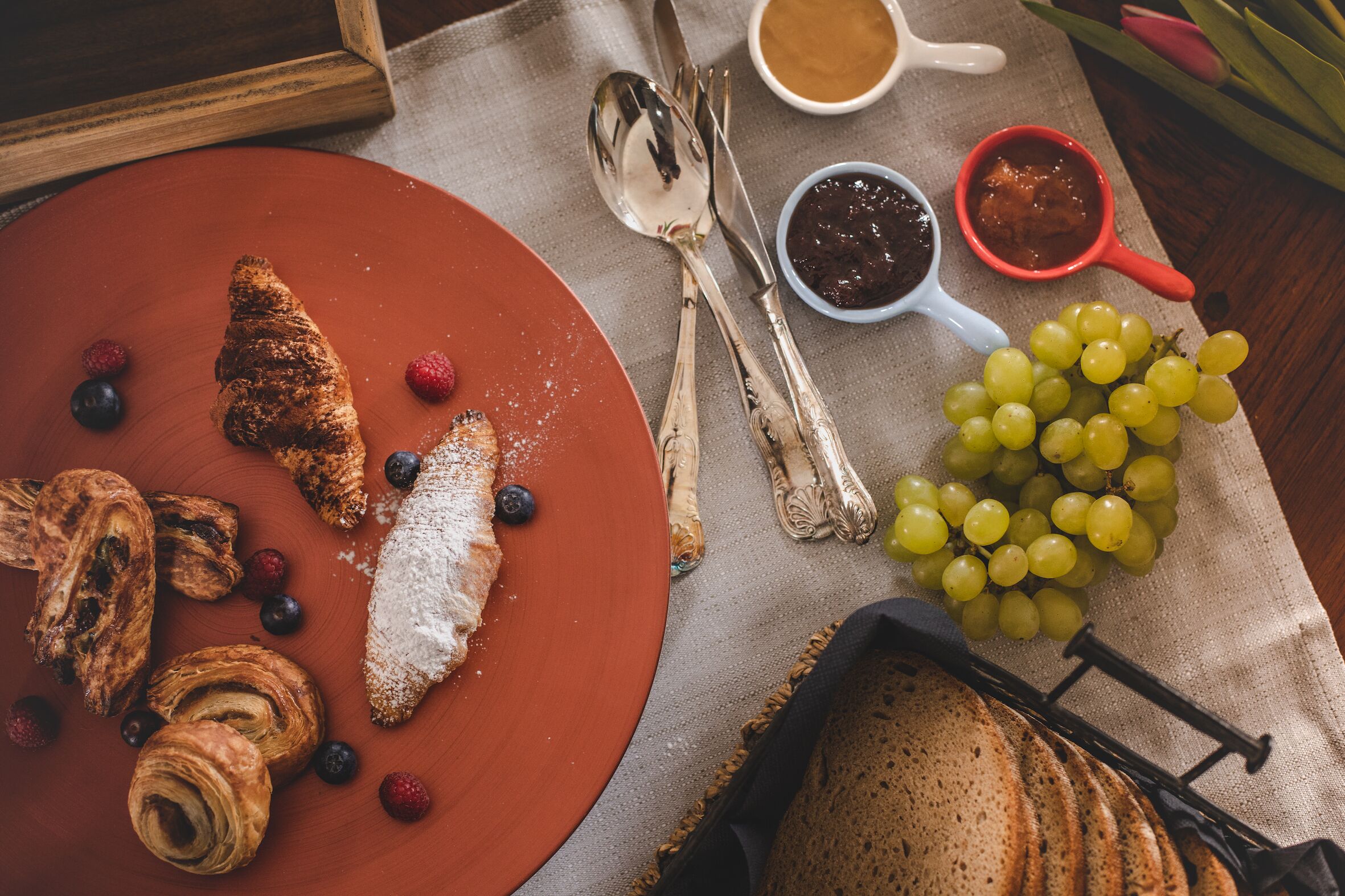 Una mesa con bollería, frutas y salsas para el desayuno.