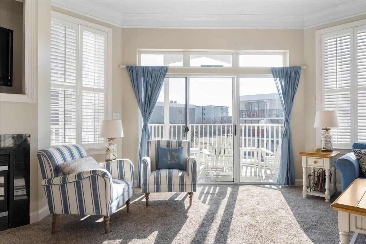 Een woonkamer met gestreepte fauteuils, een open haard, een balkon met witte leuningen en uitzicht op gebouwen.