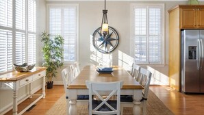 Un coin repas avec une table en bois, des chaises blanches, un luminaire suspendu et un réfrigérateur.