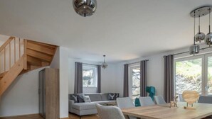 Amplia sala de estar con una escalera de madera, un sofá gris y una mesa de comedor con sillas.