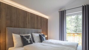 Una cama doble con ropa blanca y dos almohadones decorativos, un cabecero de madera y una ventana con cortinas.