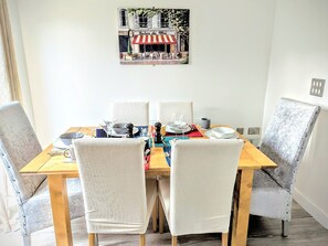 Een eettafel met vier stoelen, daarboven een schilderij en een raam aan de linkerkant.