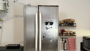 A stainless steel refrigerator with a cartoon face sticker, a kitchen counter, a microwave, and a small shelf with kitchen items. - Refuge of Lambrate - Milano Centrale (Milano)