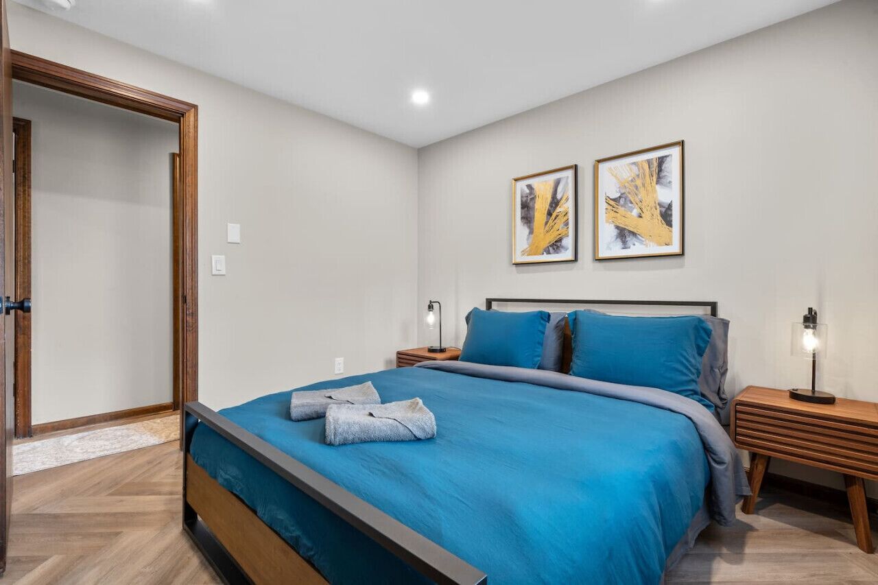 A bedroom with a bed, two bedside tables, a nightstand, and two wall-mounted artworks.