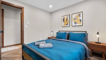 A bedroom with a bed, two bedside tables, a nightstand, and two wall-mounted artworks.