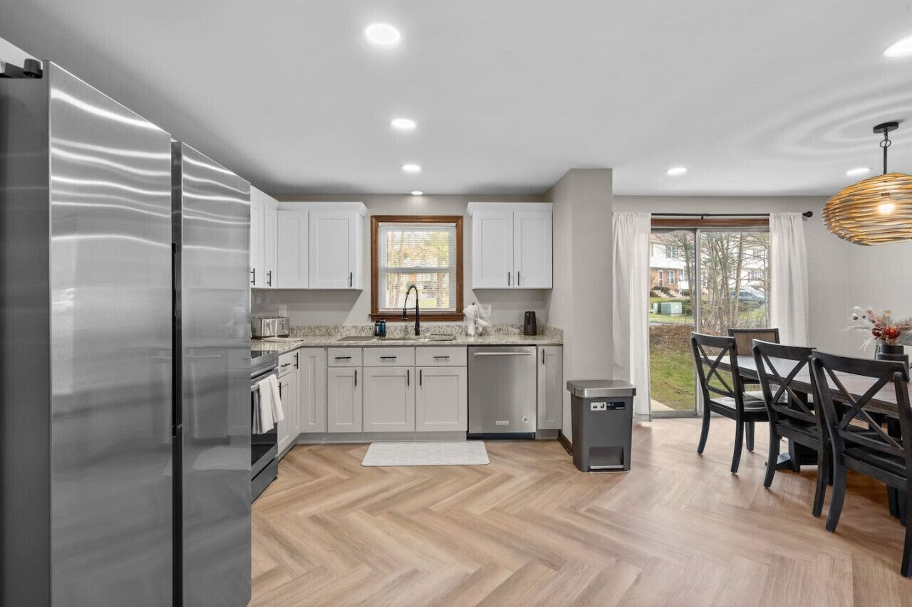 Una cocina moderna con refrigerador, gabinetes, un lavaplatos y una zona de comedor con sillas y una mesa.