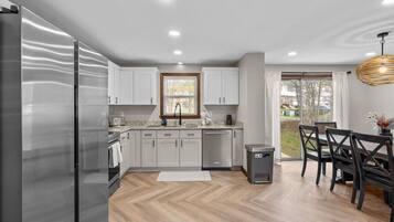Una cocina moderna con refrigerador, gabinetes, un lavaplatos y una zona de comedor con sillas y una mesa.