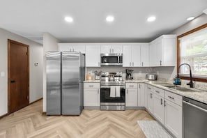 A modern kitchen with white cabinets, stainless steel appliances, and a herringbone wood floor. - #29 - Modern 5 Bedroom/2 Bath (Middletown)