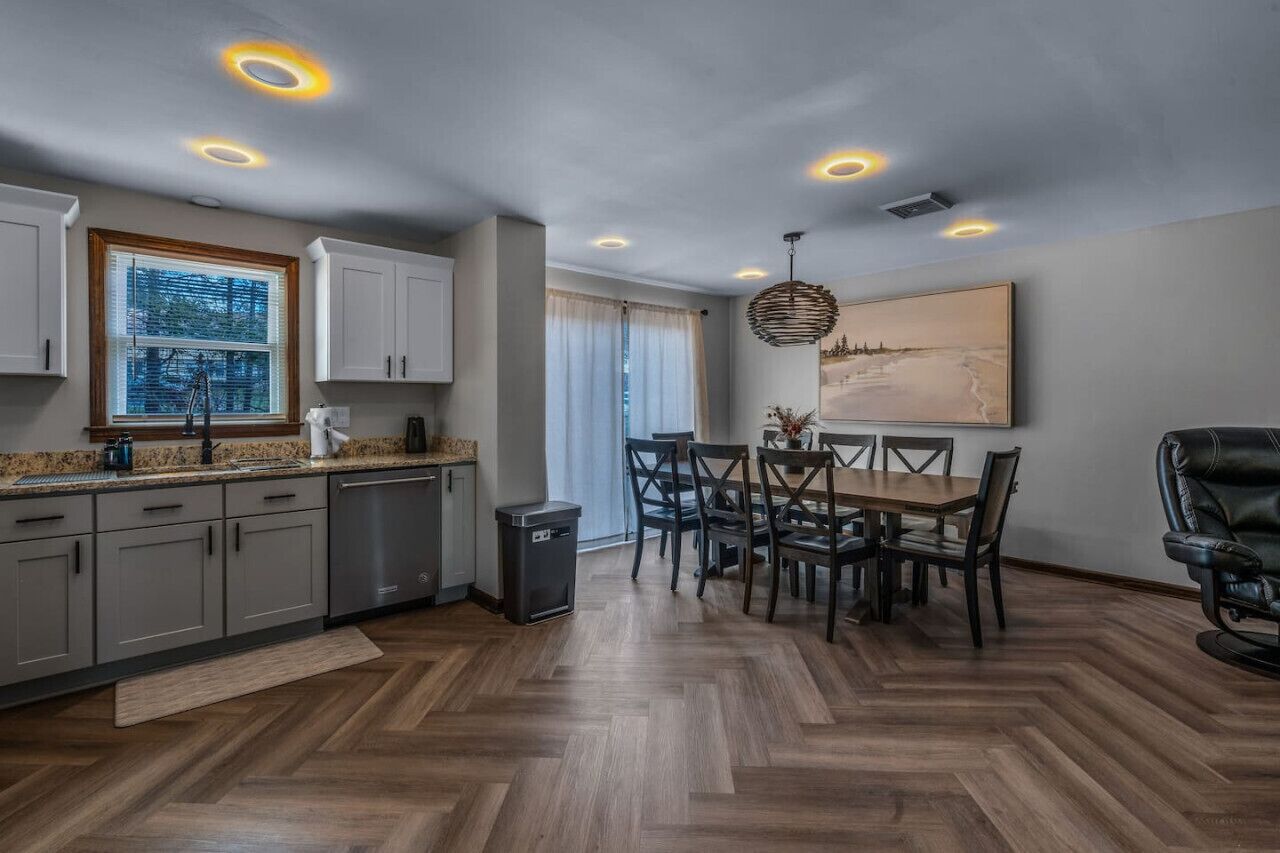 A modern kitchen with a dining area, wooden flooring, and recessed ceiling lights.