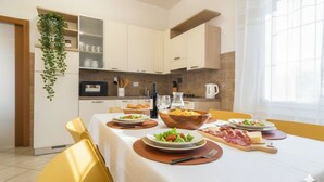 Una cocina moderna con armarios blancos, una planta colgante y una mesa de comedor con platos de comida.