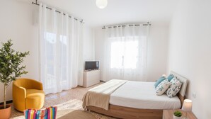 Un dormitorio con cama, televisor, planta, silla y bolso.