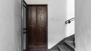 Ein schmaler Korridor mit einer Holztür, einem schwarzen Metallgitter und einer Treppe, die zu einer oberen Etage führt.