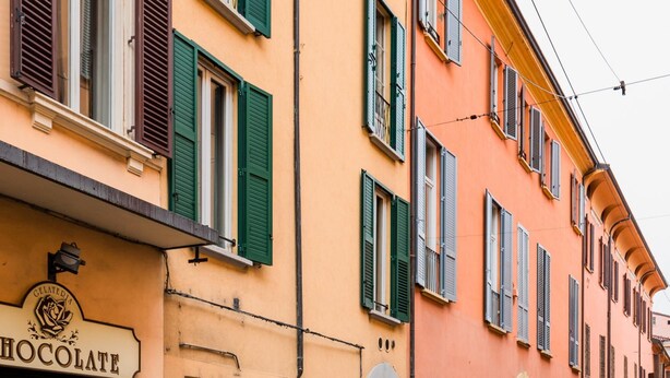 Eine Straße mit Gebäuden, die grüne Fensterläden und ein Schild mit der Aufschrift 'CHOCOLATE' zeigen.